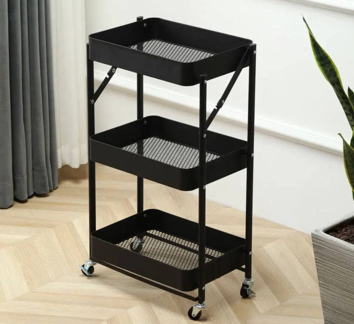 Chariot 3 Étagère noir en métal, avec trois paniers à fond grillagé et des roulettes pivotantes pour le rangement.